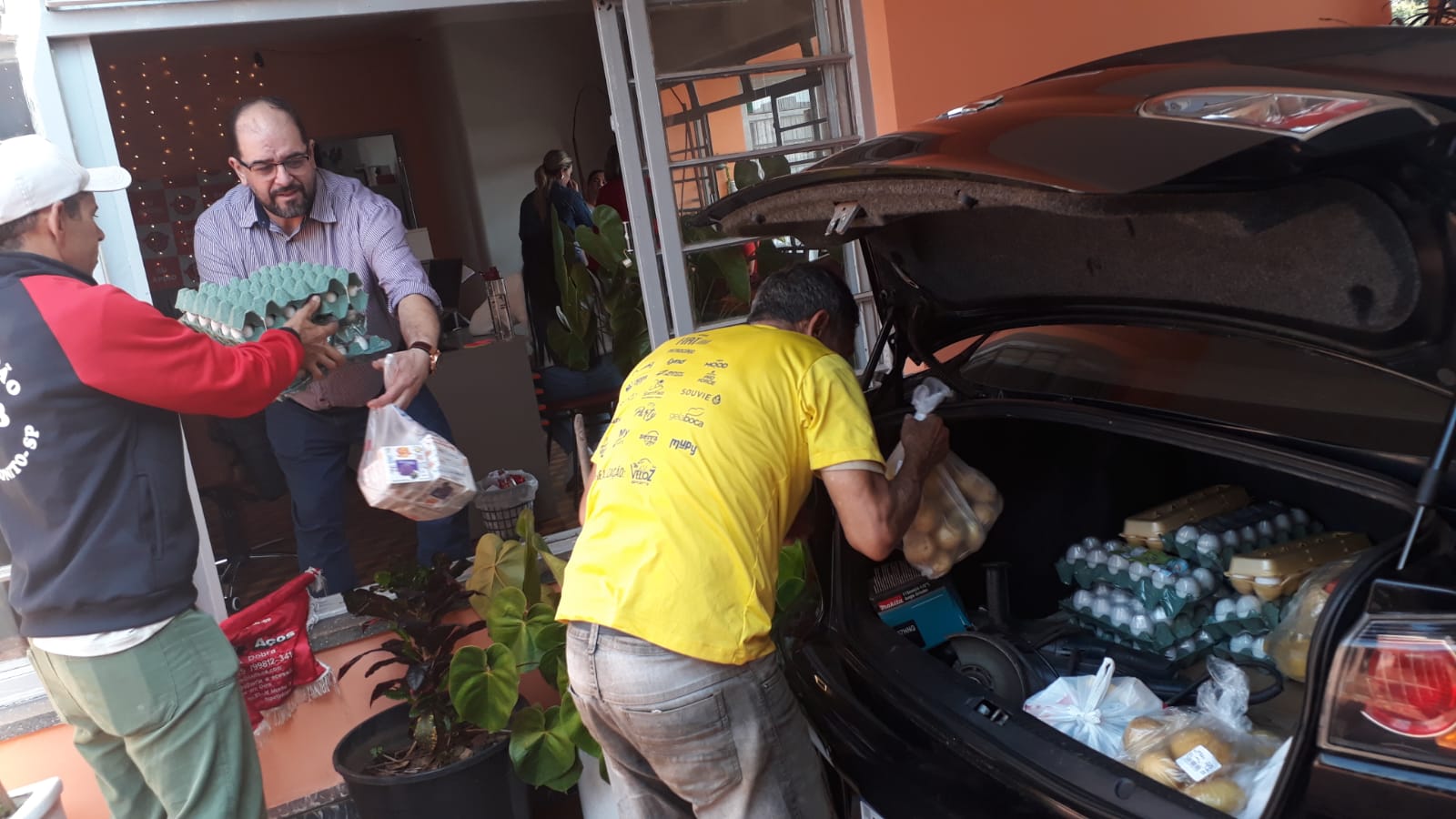 Voluntários da ACCB carregando os alimentos doados no porta-malas de um carro